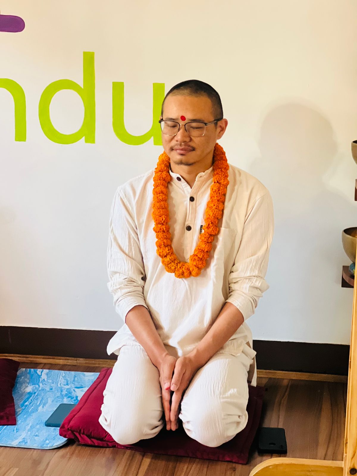 Meditation teacher seated in white kurta with marigold garland, Kathmandu